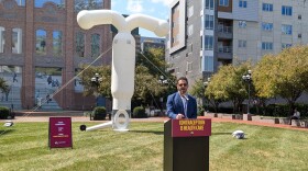 A man speaks at a podium in front of what appears to be a giant inflatable intrauterine device.