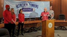 A man speaks at a podium, in front of a banner reading "Bethlehem Running Festival"