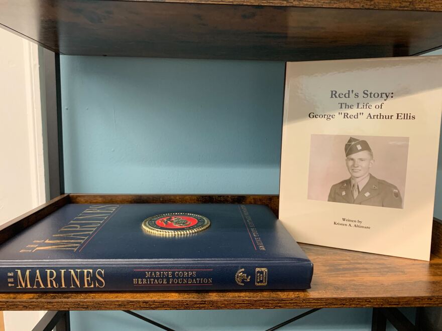 A book, "The Marines: Marine Corps Heritage Foundation," on a bookshelf.