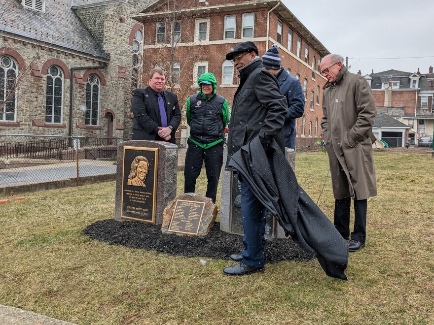 Five people in winter clothes gather around a stone monument to Martin Luther King Jr and his wife Coretta Scott King. It looks like two rounded headstones with a small plaque in the middle