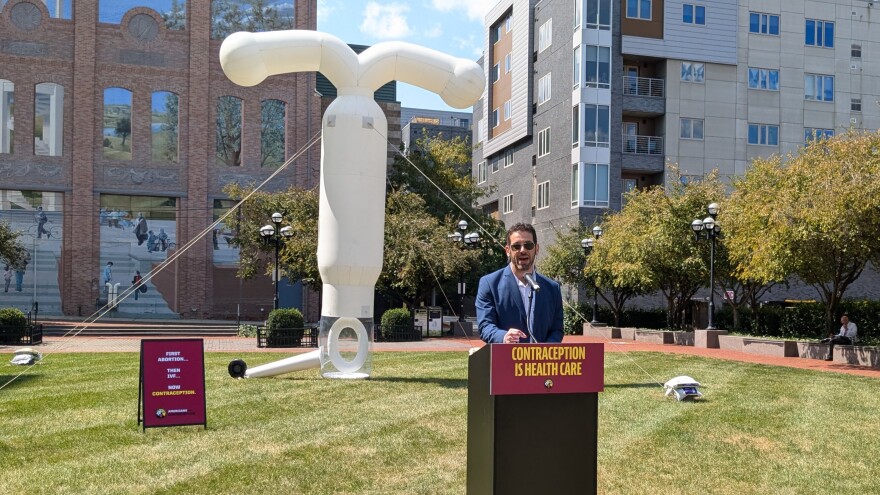A man speaks at a podium in front of what appears to be a giant inflatable intrauterine device.