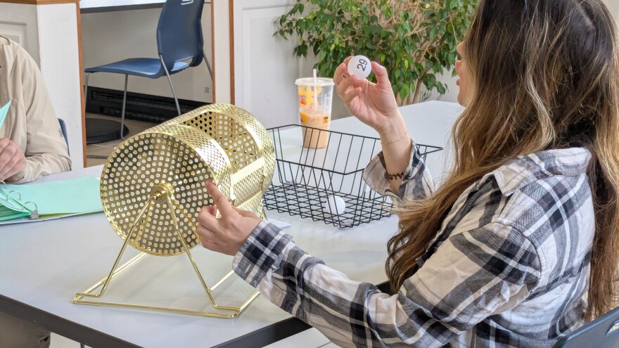 A woman pulls a ping pong ball with "29" written on it from a gold tumbler.