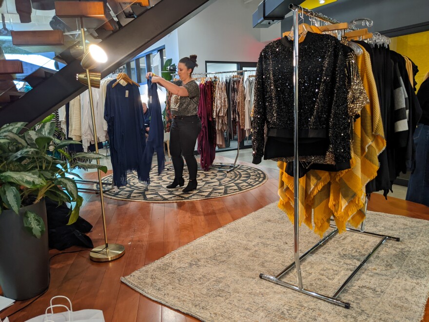 An attendee is in the middle of a set of racks that each have different clothing designs by Lara Bly. She holds a blue shirt up to look at.