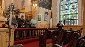 A woman holding sheet of paper speaks in front of a large Gothic stained glass window