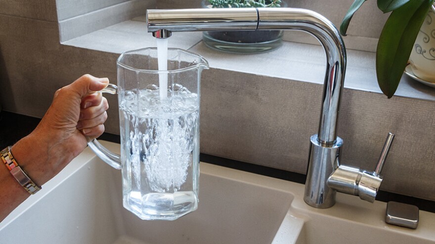 A pitcher is filled with tap water at a sink