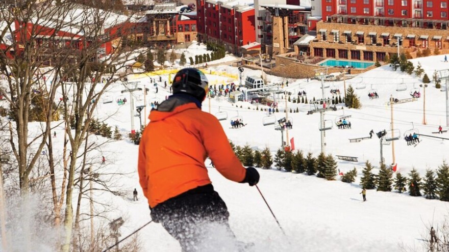 A skier on top of a slope wearing a red jacket and black hat