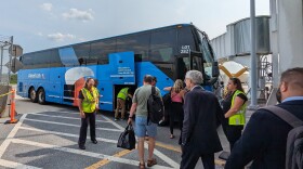 Passengers boarding a blue bus with the American Airlines logo, as workers in bright orange safety vests assist.