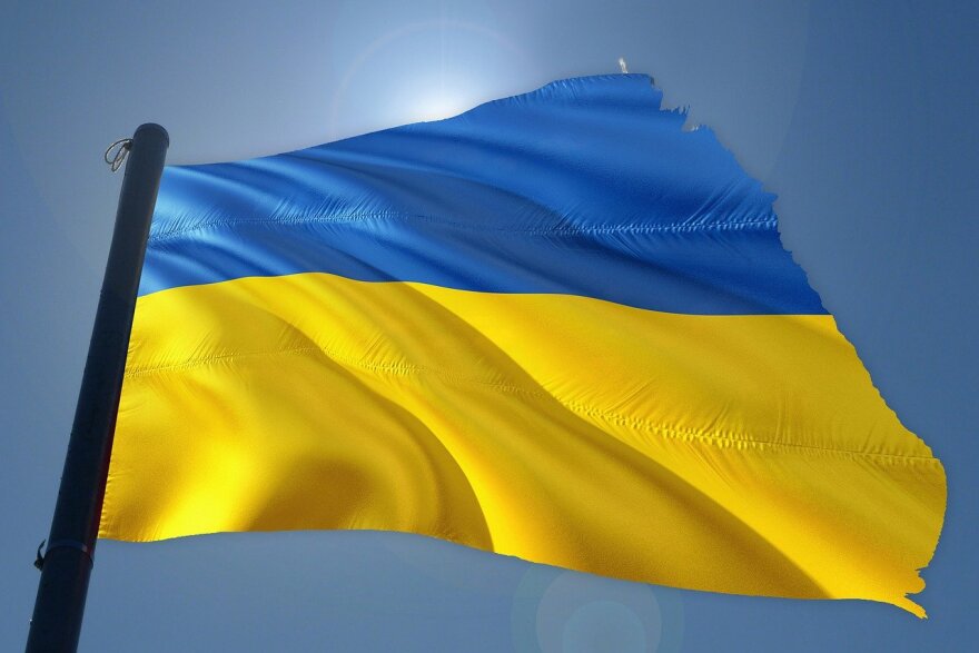 Ukrainian flag with blue stripe on top and golden yellow on bottom in a blue sky.