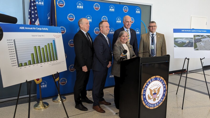 Five politicians stand behind a podium smiling.