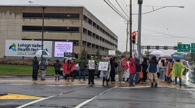 About two dozen people, many with signs like "fire Jenssen," stand in the rain in front of a Lehigh Valley Health Network sign.