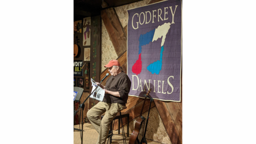 A man on a stool reads a book into a microphone