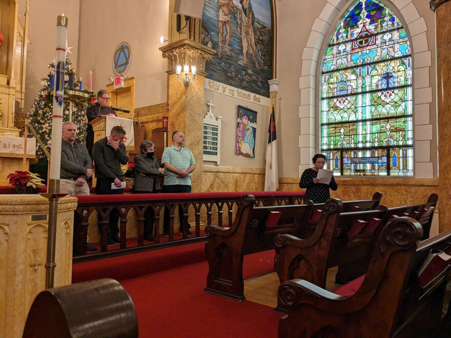 A woman holding sheet of paper speaks in front of a large Gothic stained glass window