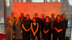 People in semiformal clothing standing in front of a step and repeat.