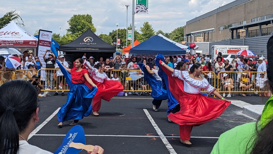 Dancers in red and blue dresses with big, flowing skirts dance in front of a crowd
