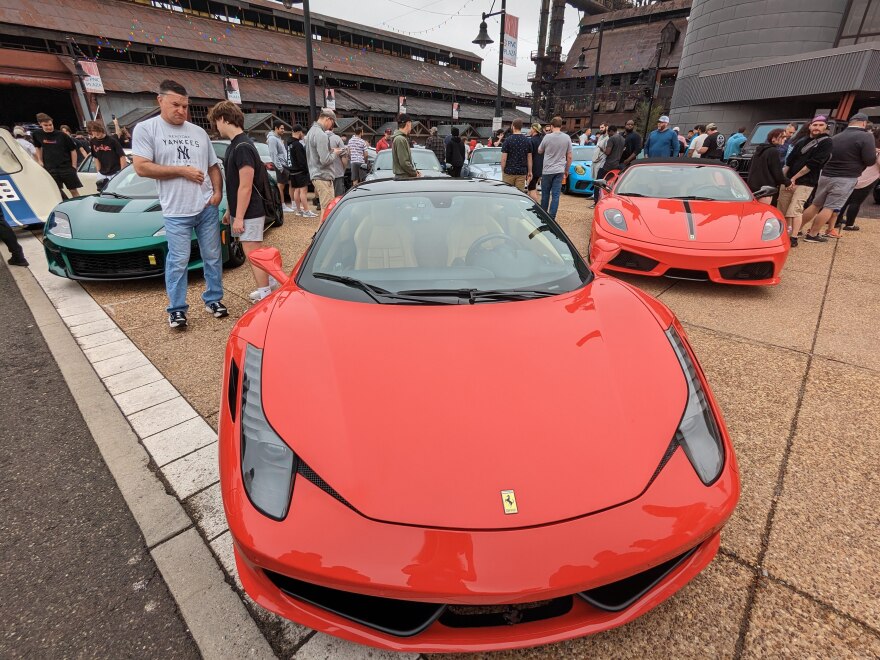 Two red Ferraris and a dark-green Lotus sports car, surrounded by onlookers.