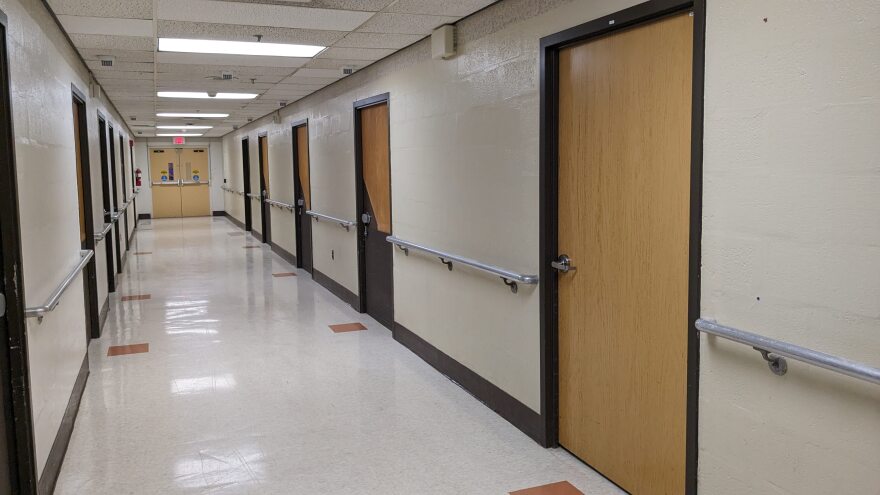 A mostly white hallway with 10 wooden doors, five on each side.