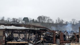 A burnt-out building with collapsing roof, with bits of white smoke still rising.